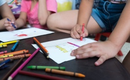 Dzieci kolorują, na stole leżą kartki i kredki