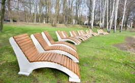 Leżaki betonowe stojące przy stawie Maciek, w tle drzewa